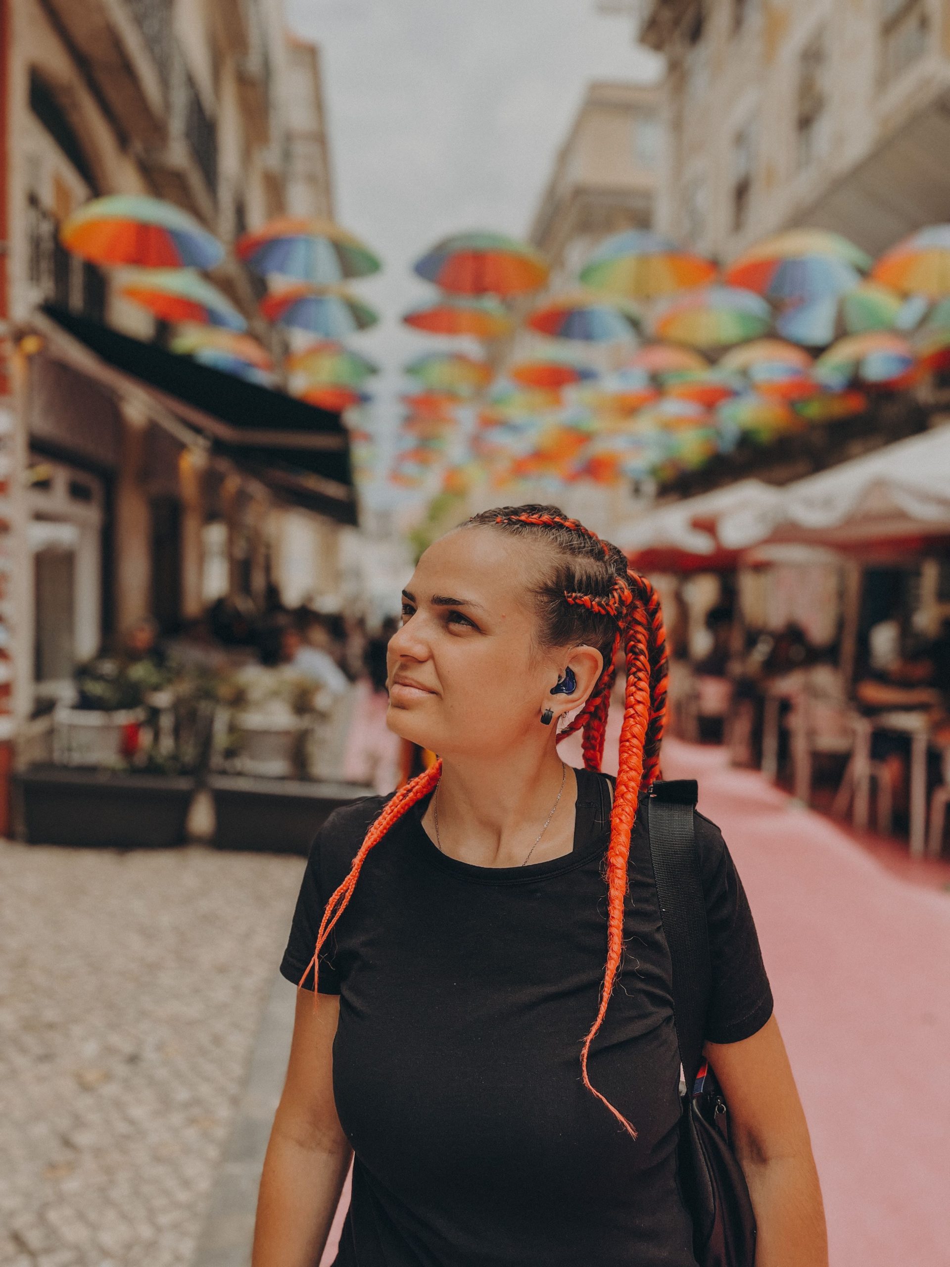 Zdjęcie przestawia zamyśloną Olesię Vasichkina ma zaplecione włosy na tle ulicy pełnej kolorowych parasoli.