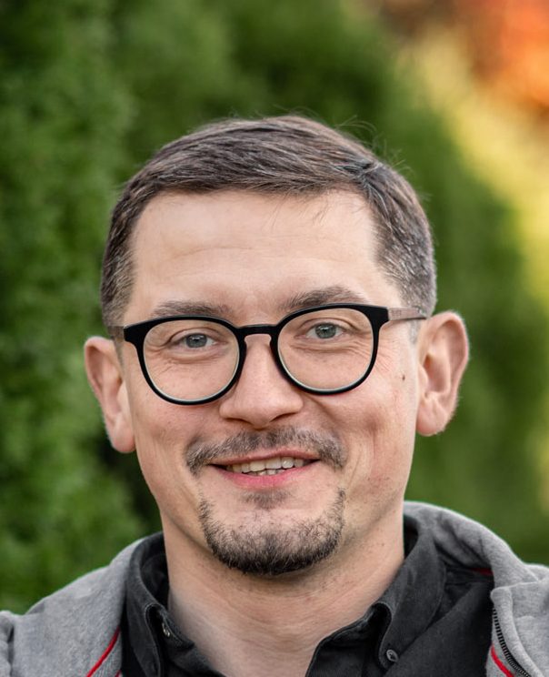 Portret Tomasza Grabowskiego, uśmiecha się, na tle parku