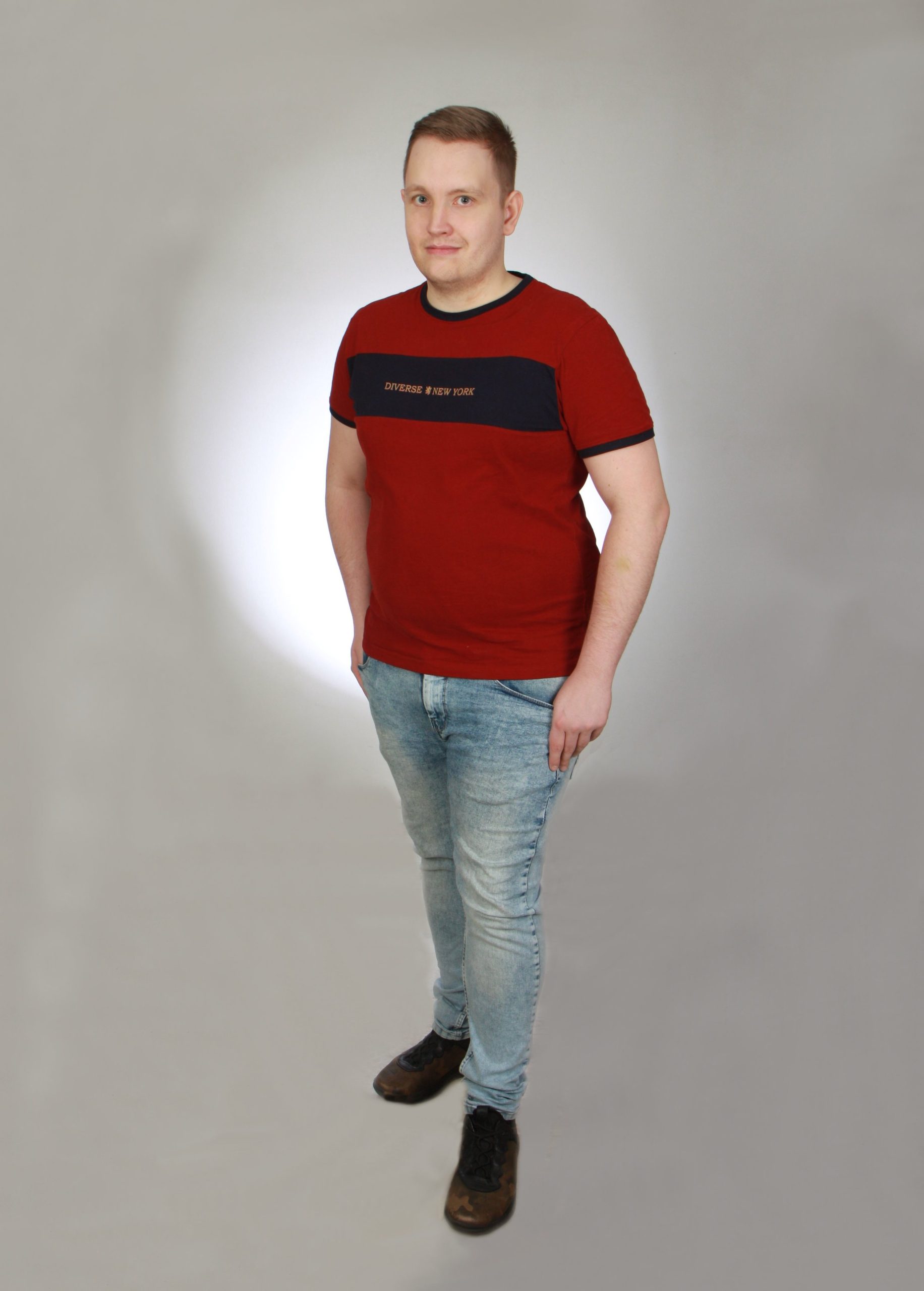 Zdjęcie Tomka - młodego mężczyzny ubranego z dżinsy i czerowny t-shirt. Zdjęcie zrobione w studio, na białym tle.